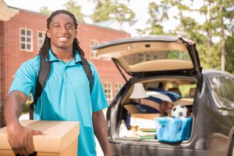Young male heads off to college. The 18-year-old is unpacking his car as he moves into the college campus dorm. He is excited to start his school adventures. He carries a backpack and moving box. Back to school.