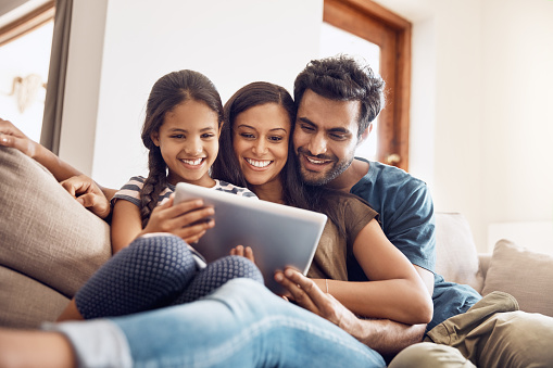 Shot of a mother and father using a digital tablet with their daughter on the sofa at home