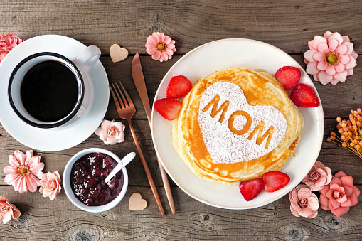 Show Mom Love! Pancakes with heart shape and MOM letters. Mother's Day breakfast concept. Overhead view table scene with a rustic wood background.