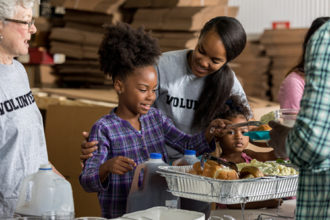 A young mother and her two little girls serve a healthy meal to people in a homeless shelter.