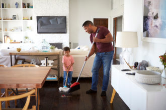 Grandfather and his three year old grandson mopping and sweeping the dining room floor, full length