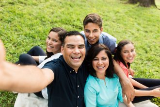Father's Day - A happy latin family of five taking a selfie and smiling in a horizontal medium shot outdoors.