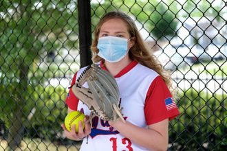 Youth Sports and COVID-19: Teenage girl in her softball uniform posing with a healthcare mask to protect her from the Coronavirus