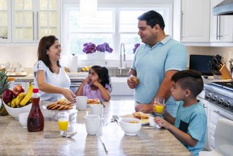 Reset Schedule - Hispanic parents enjoying breakfast with their young son and daughter in their kitchen.