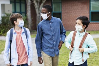 Back-to-school hacks: A multi-ethnic group of three middle school students walking and conversing outside the school building, carrying backpacks. The three boys are back to school during the COVID-19 pandemic, wearing protective face masks to help prevent the spread of coronavirus. The two shorter ones are brothers, mixed race Asian and Caucasian, 11 and 12 years old.