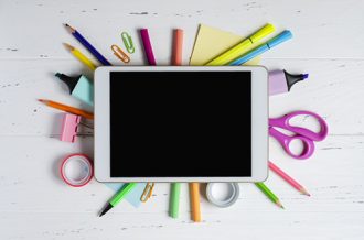 School tech accessories: tablet with an empty screen and office supplies on a white wooden background. Concept app for school children or online learning for children.