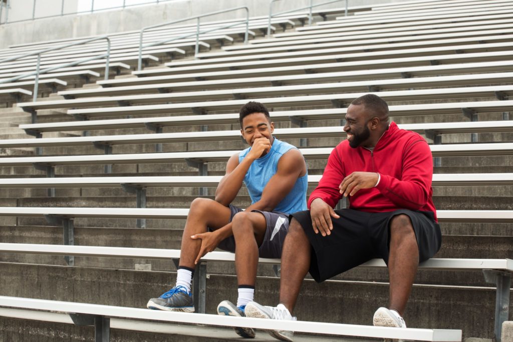 A student athlete and mentor sit on the bleachers