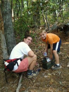 Shown here are a mother (30 something) and her six-year-old son finding a hidden treasure while geocaching in the woods. Geocaching is a treasure hunting game where you use a GPS to hide and seek containers with other participants in the activity. All logos removed.
