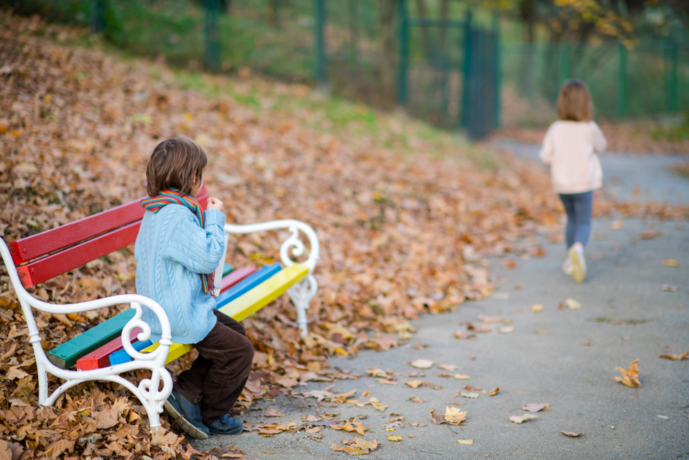 Child sitting on bench with friend walking away